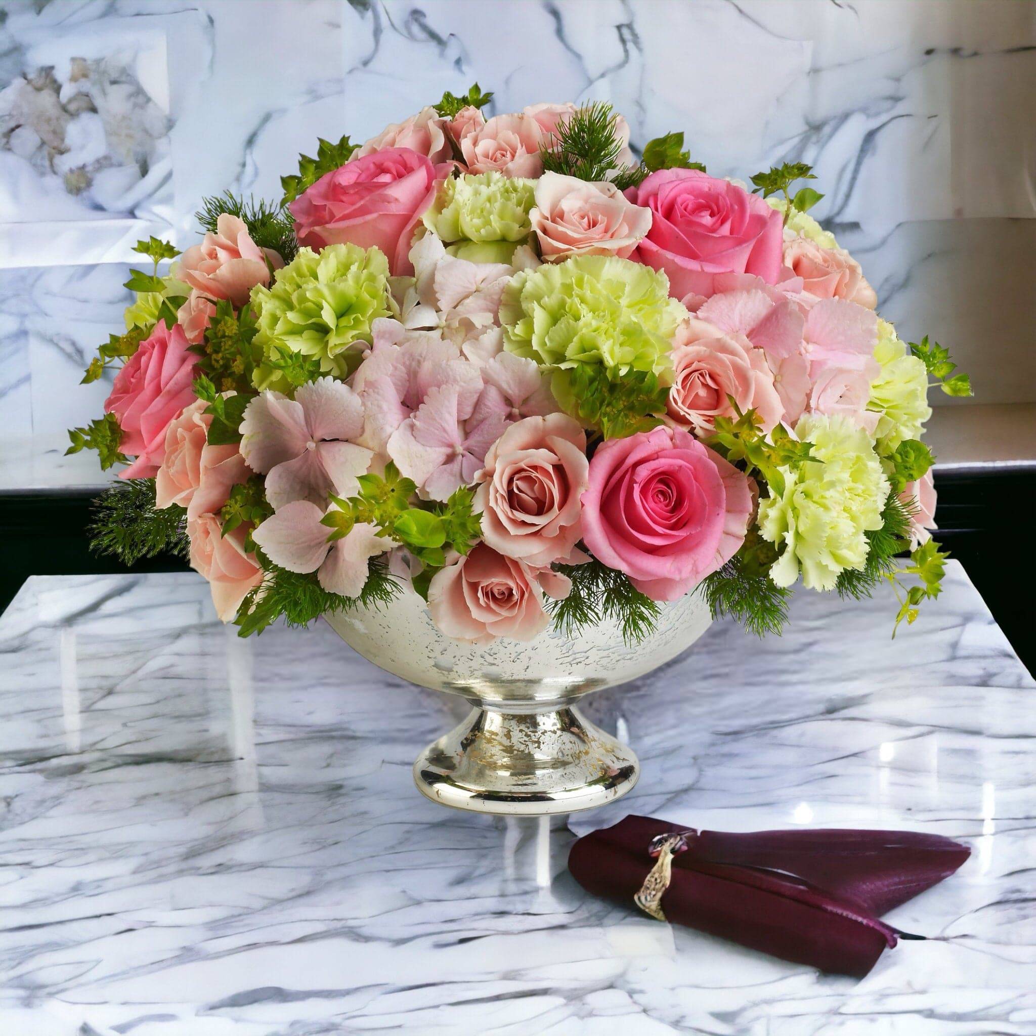 Low arrangement of pink roses, pale hydrangeas, and green carnations in a silver compote vase