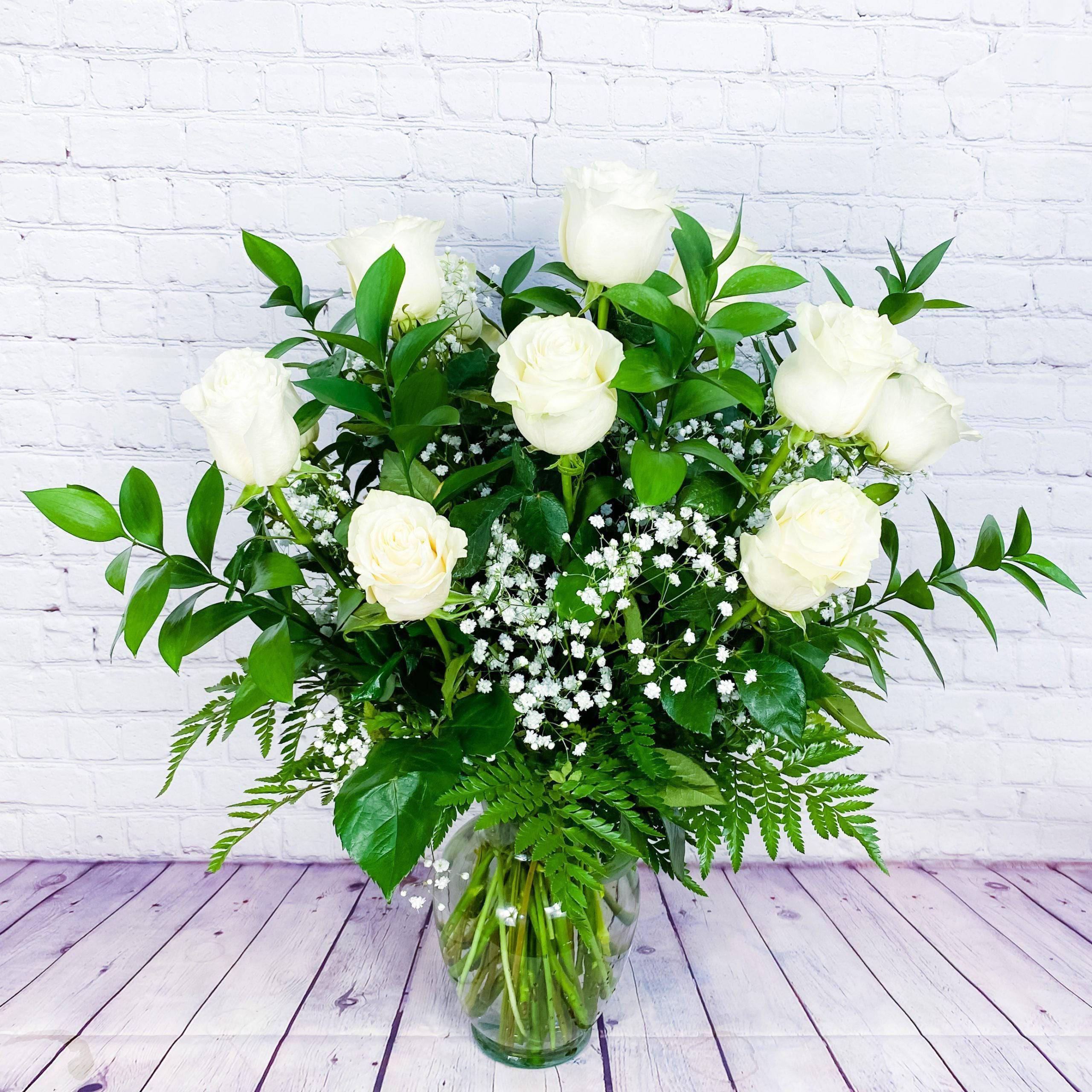 White roses in a glass vase with baby's breath and greenery