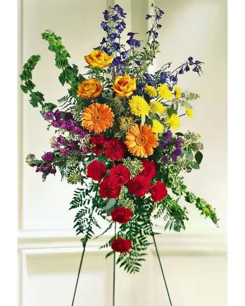 Tall standing spray on an easel with bright red, yellow, orange, and purple flowers.