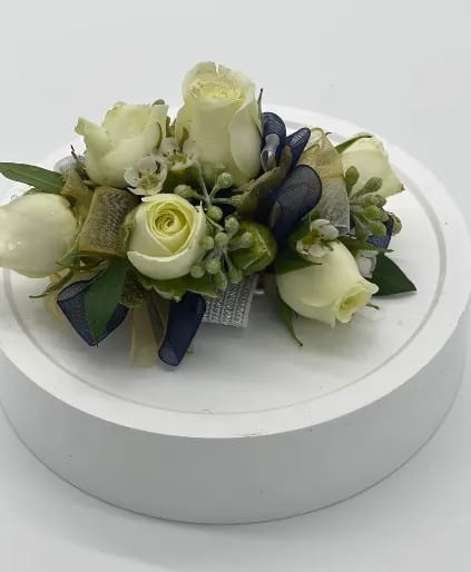 Wrist corsage of ivory roses with navy and gold ribbon on a rhinestone bracelet band