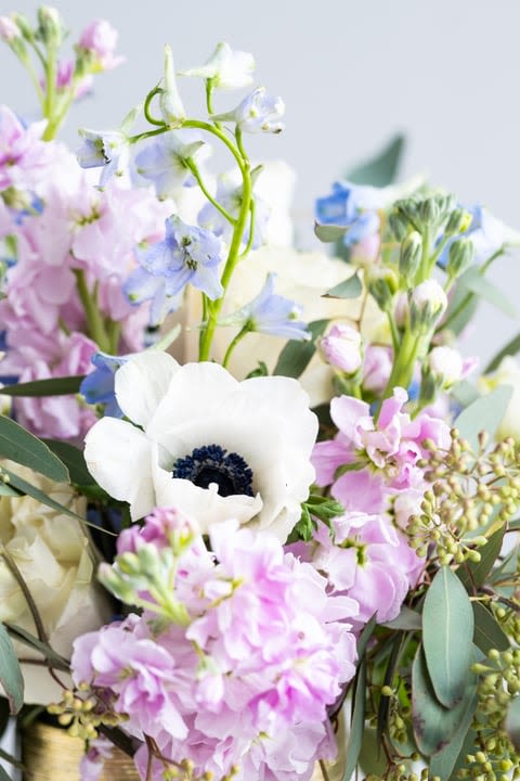 Pastel bouquet with white anemone, pink stock, and light blue delphinium flowers.