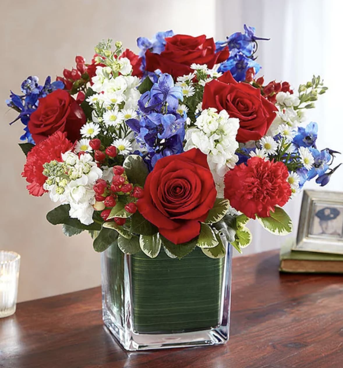 Red, White and Blue Cube - Our arrangement of red roses, white stock, and blue delphinium, expertly gathered in a clear glass cube lined with Ti leaf ribbon, makes for a respectful and exquisite gesture of comfort and healing.