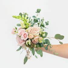 Handheld bouquet of blush pink roses and white flowers with airy greenery against a white background.