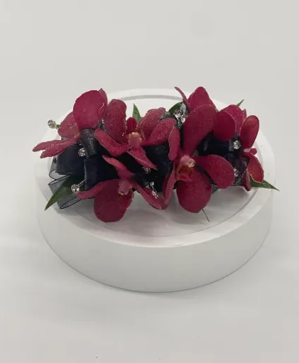 Red orchid wrist corsage with black ribbon and rhinestone accents on a white stand
