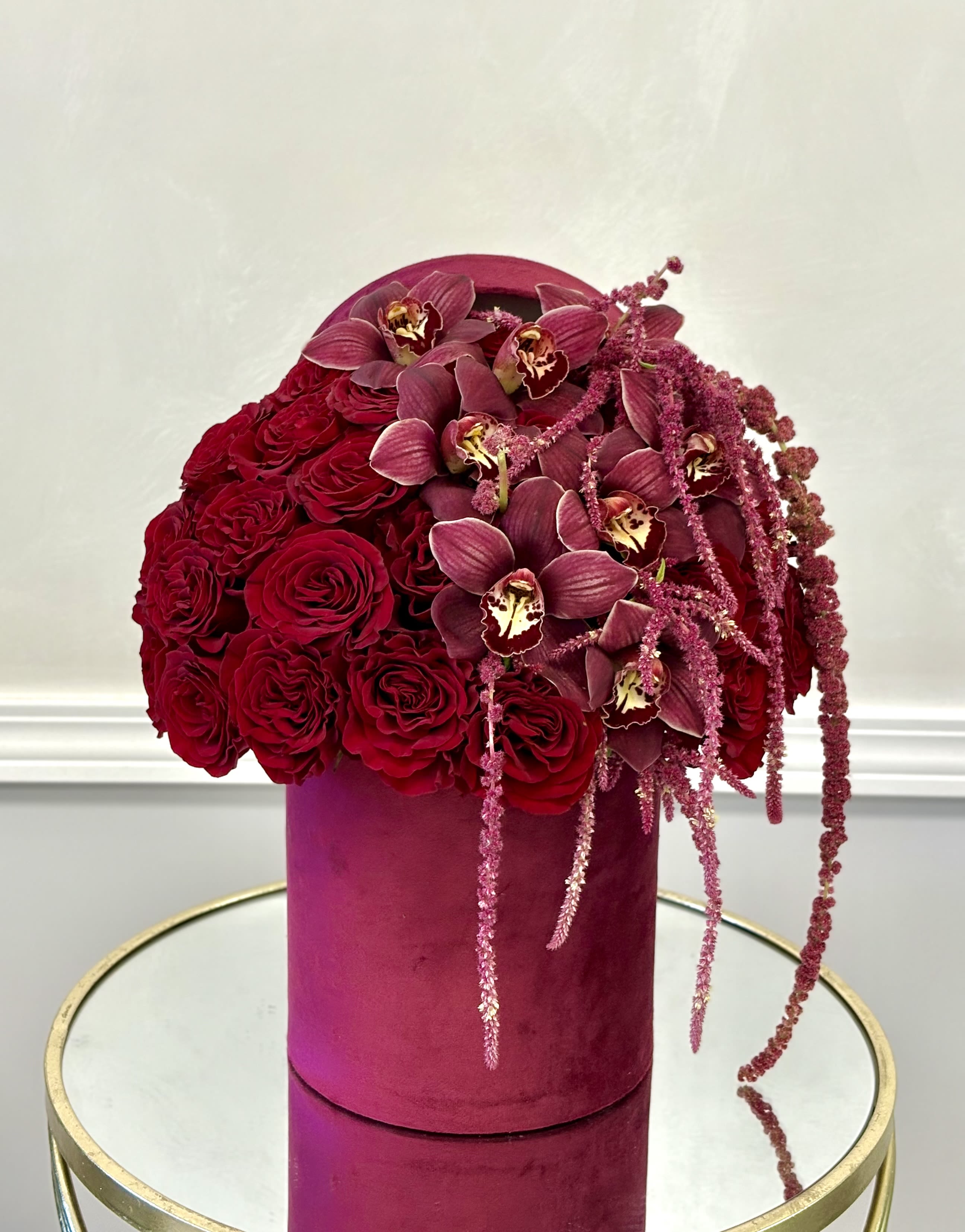 Royal Red Luxe By VLM Flowers - A luxurious blend of deep red roses and rich burgundy orchids, accented with cascading amaranthus for added drama and movement. Presented in a velvet box, this arrangement delivers a bold, elegant statement perfect for unforgettable moments.