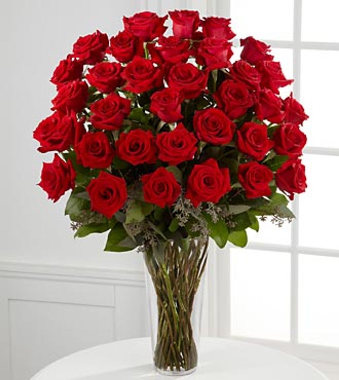 Tall arrangement of many red roses in a clear glass vase