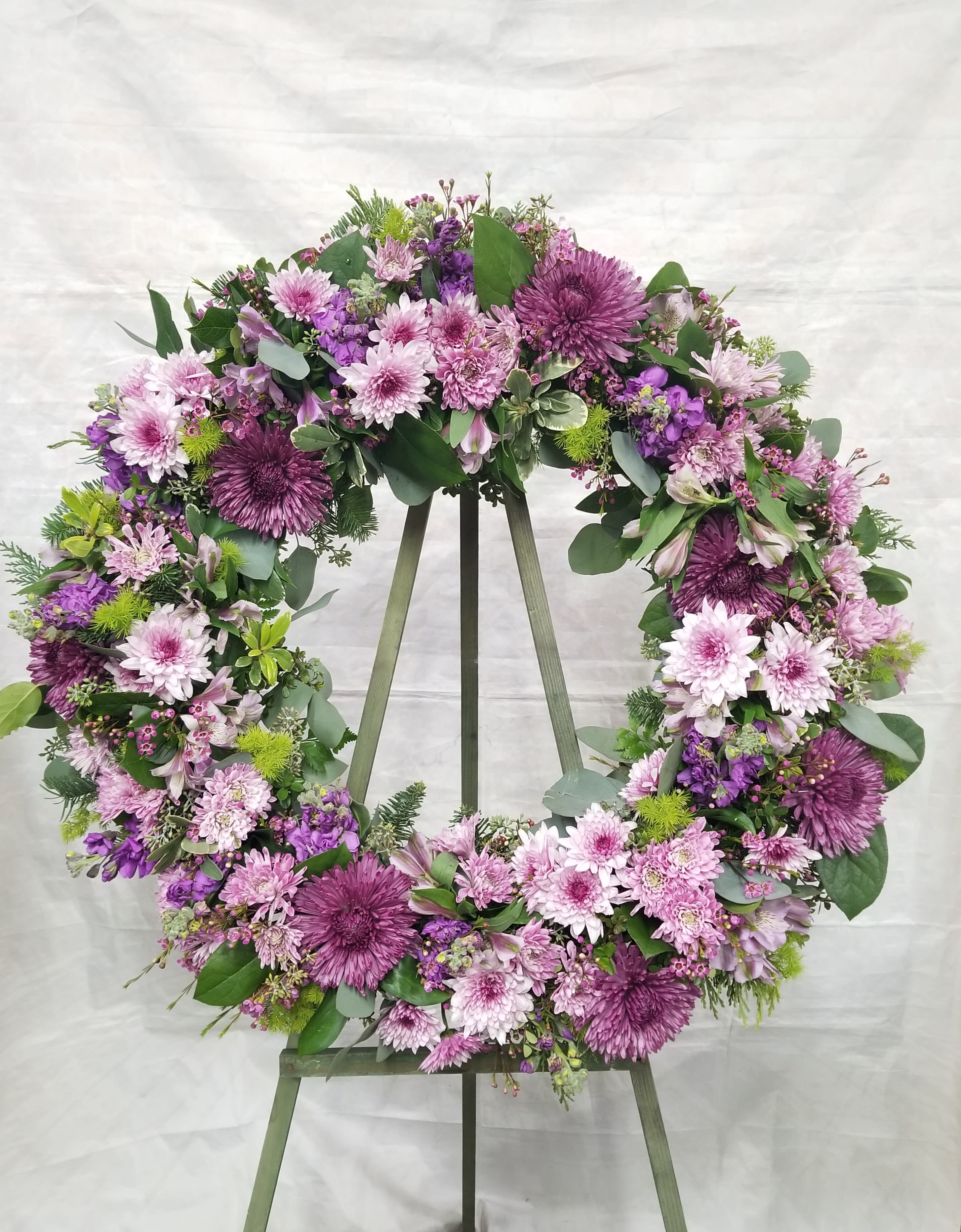 Large purple and pink floral wreath on a wooden easel against a light backdrop