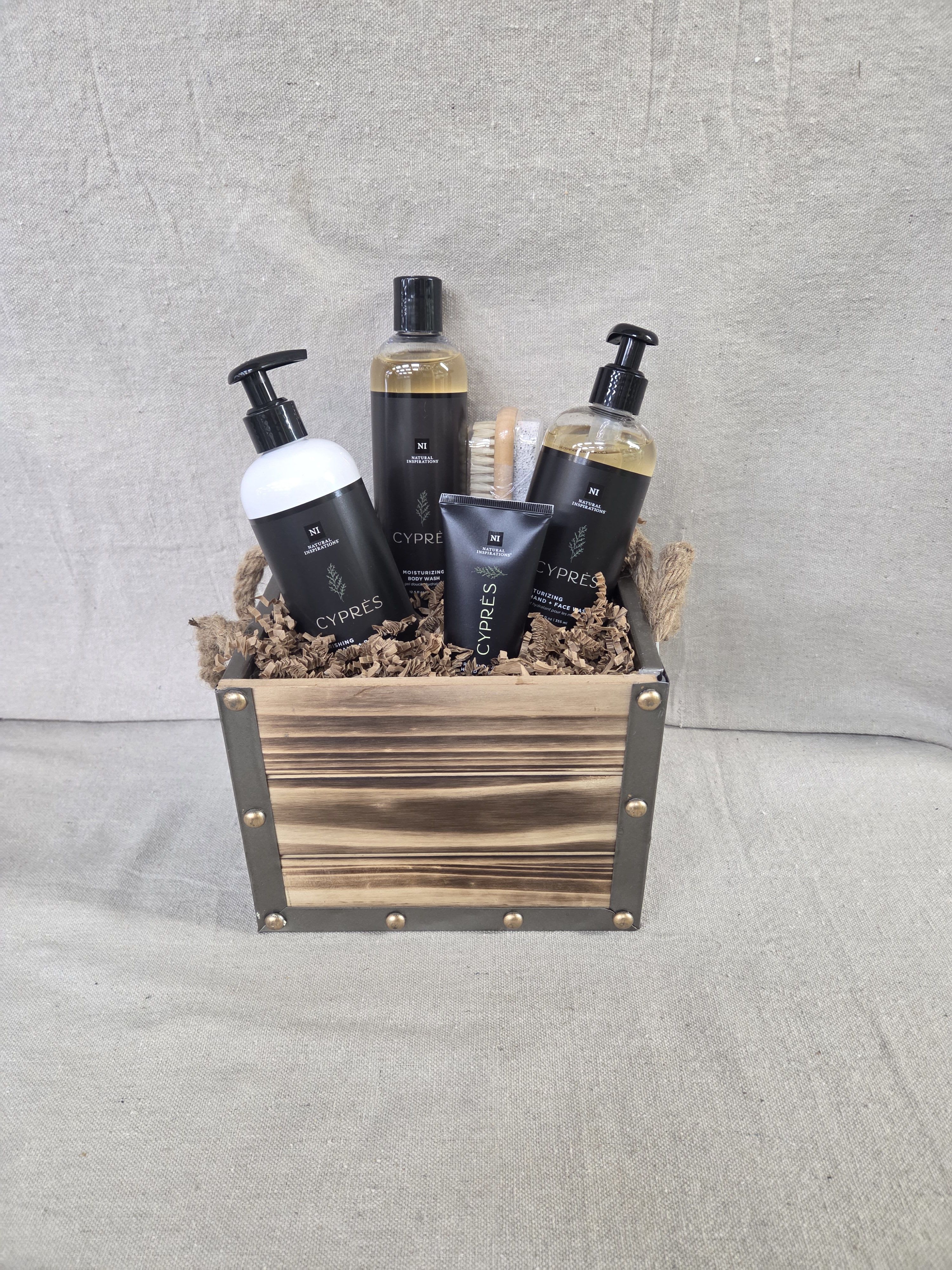Wooden crate filled with black-labeled bath products and a small brush on shredded paper filler