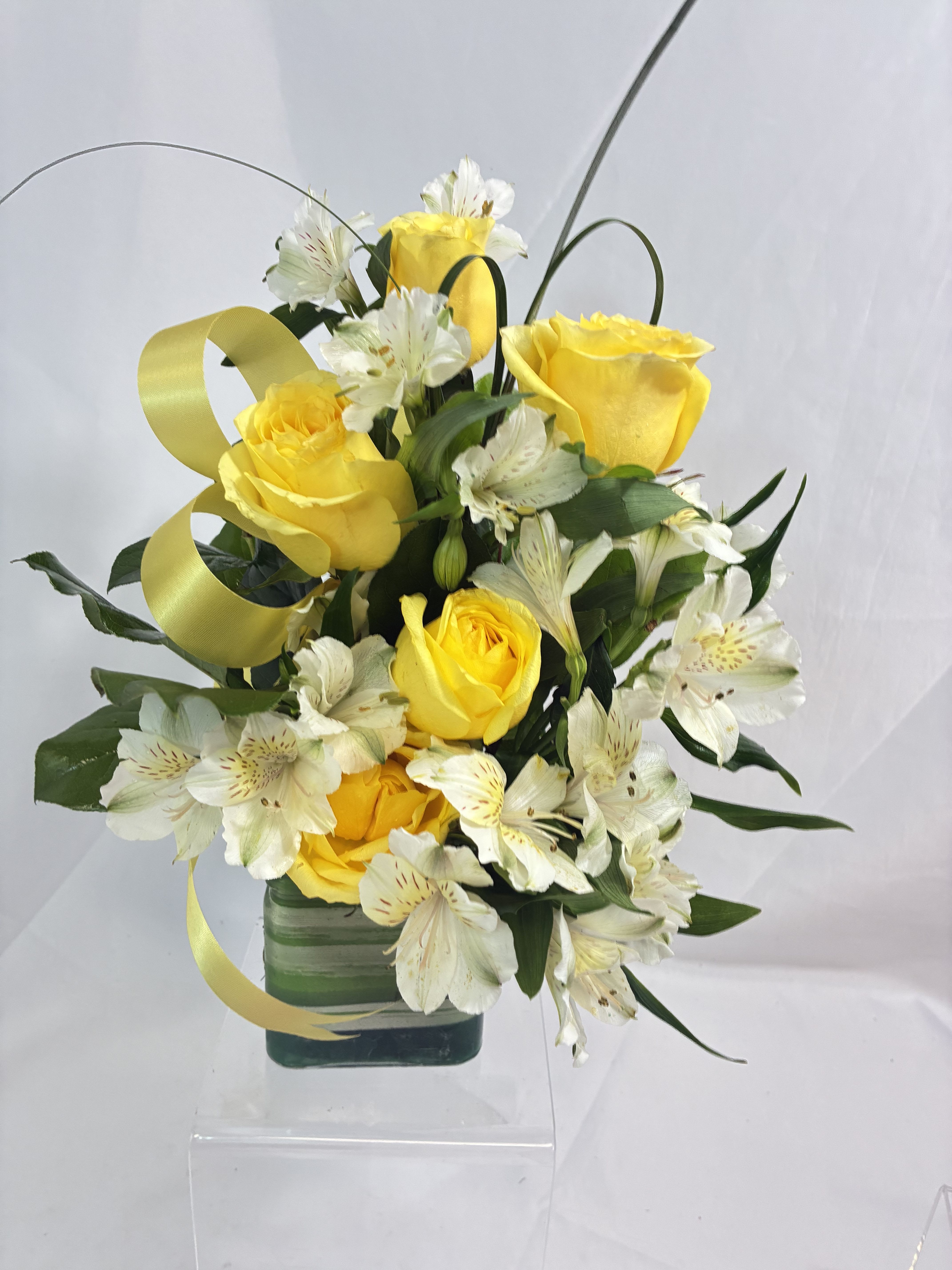 Roses of Sunshine  - Send a bit of beautiful, yellow sunshine to that special someone! These yellow Roses are sure to let them know how special they are and brighten up their day! In a glass cube, wrapped with an Aspidistra leaf, these yellow Roses are accented by white blooms all waving hello! Special touches of Bear Grass, greenery and ribbon, tie this gift of happy all up!
