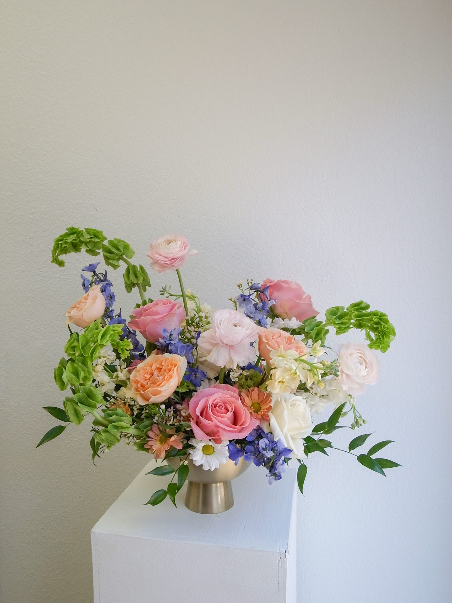 Floral Overture - A lush and vibrant composition of spring’s finest notes, Floral Overture blends bright pinks and soft blues with the graceful texture of Bells of Ireland and gorgeous lush roses. This larger, compote-style arrangement feels like a celebration in bloom—fresh, joyful, and artfully layered. Perfect for bringing energy and elegance to any space, it captures the season’s beauty in a harmonious symphony of color and texture.