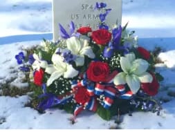 Patriotic red, white, and blue floral spray with ribbon placed at a snowy grave marker