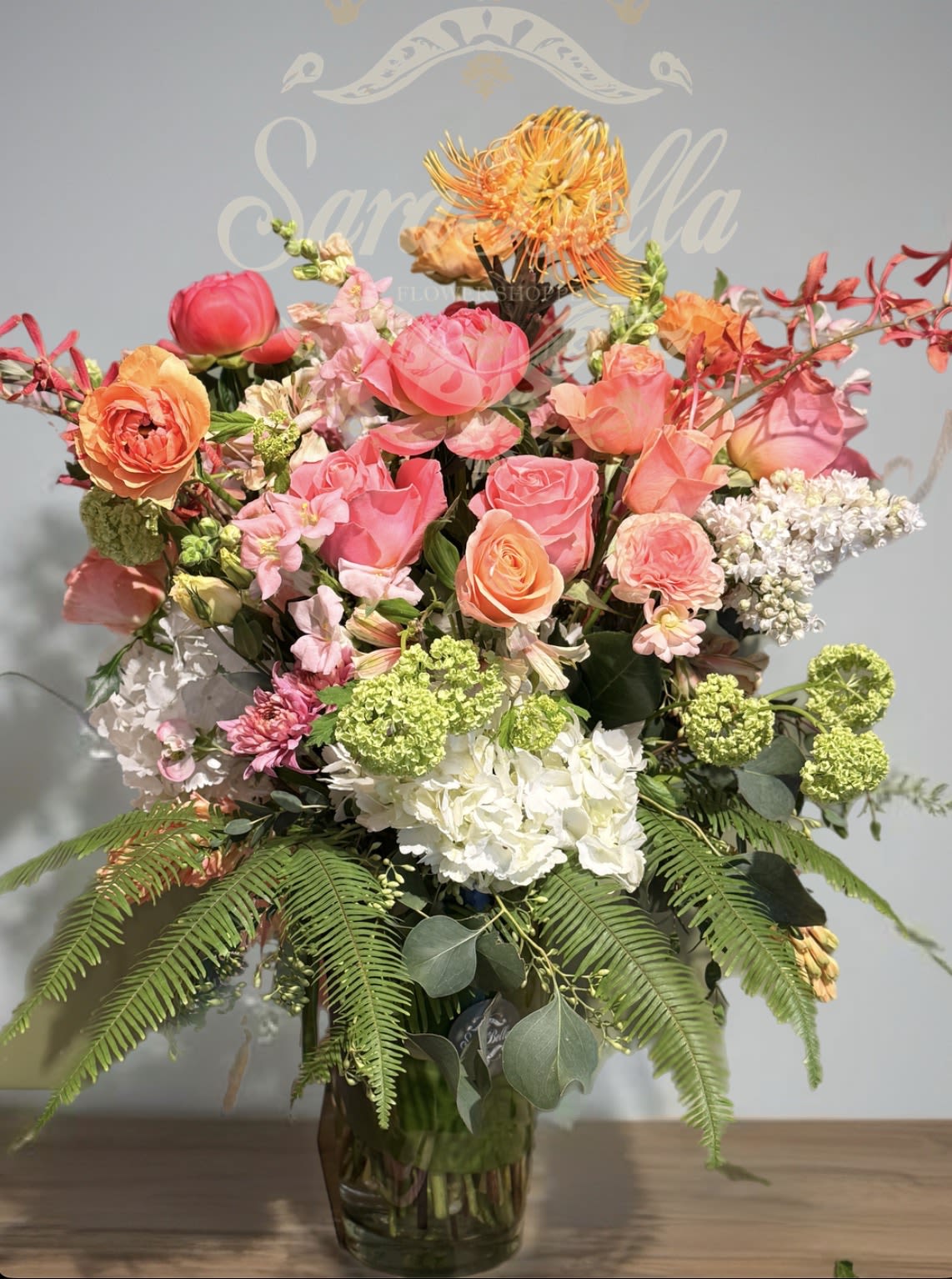 CORAL SYMPHONY  - A lively artistic arrangement bursting with texture and color,featuring,garden roses,lisianthus,hydrangea,scabiosa,and unique seasonal blooms and vibrant pink.lavender,and citrus tones....