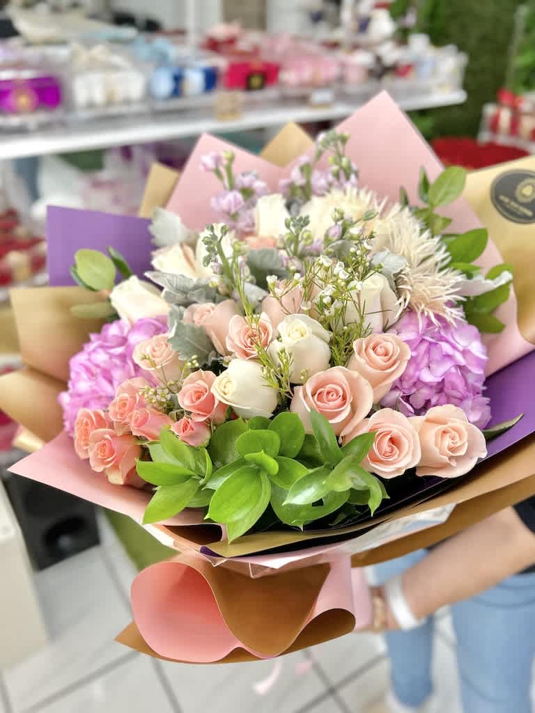 Hand-tied bouquet of pink and cream roses with hydrangeas and mixed blooms in pastel wrapping paper