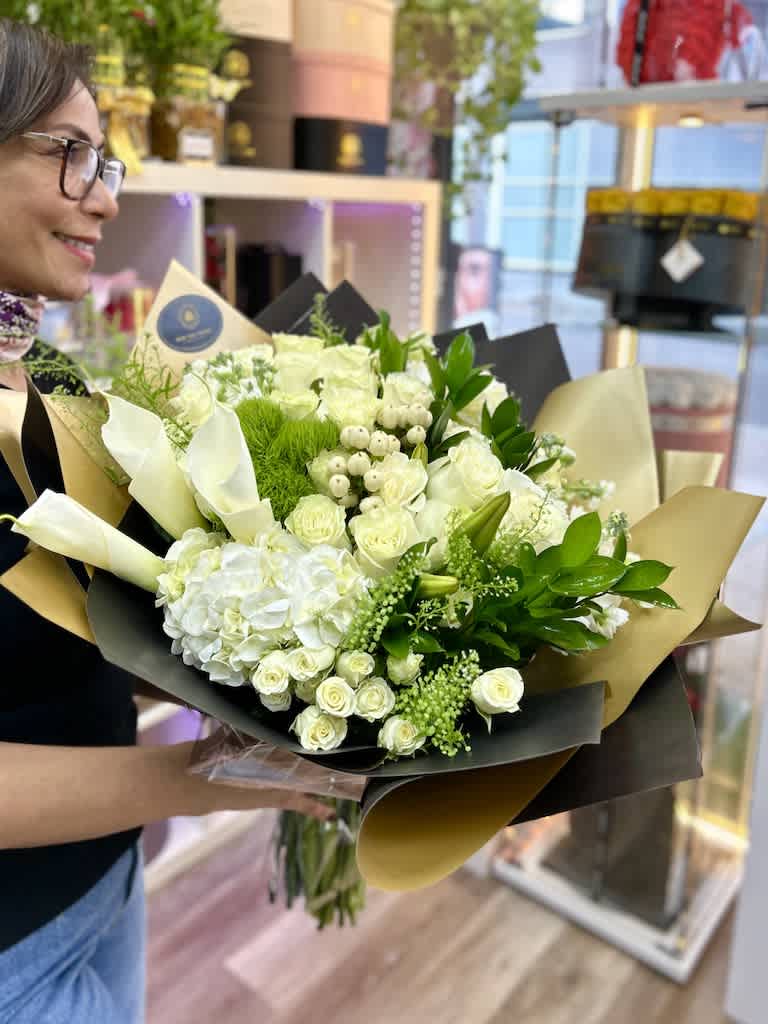 Large hand-tied bouquet of white roses, hydrangeas, and calla lilies wrapped in black and gold paper