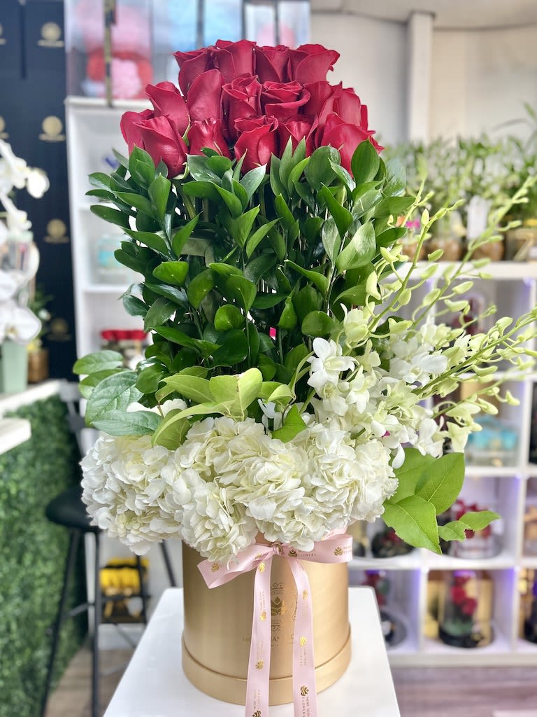 Tall arrangement of red roses and white hydrangeas in a gold hat box with pink ribbon