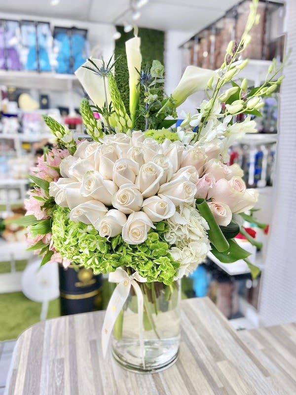 Tall arrangement of white roses, calla lilies and green hydrangeas in a clear glass vase
