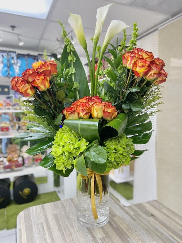 Tall arrangement of orange roses, white calla lilies, and green hydrangeas in a clear glass vase