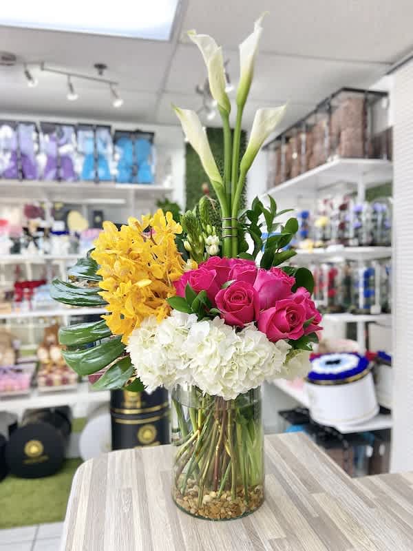 Tall arrangement of white calla lilies, yellow orchids, hot pink roses, and white hydrangeas in a glass vase