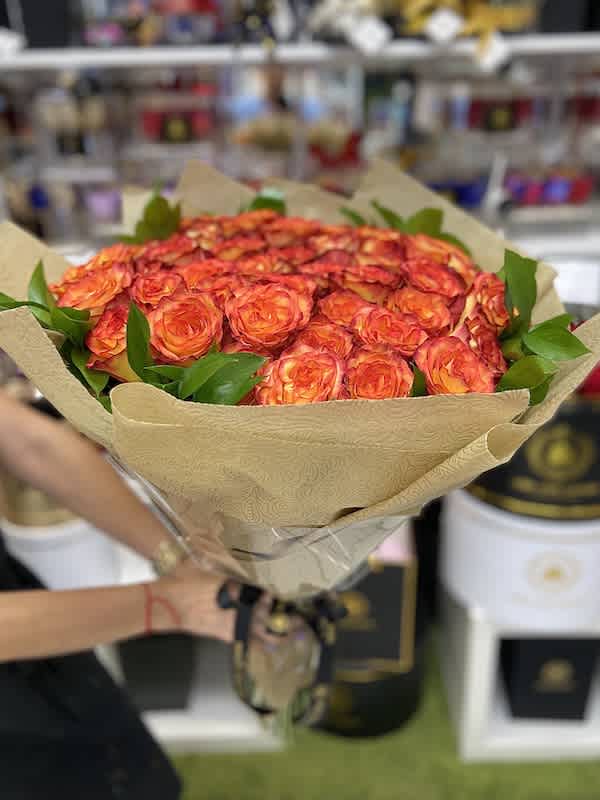 Large bouquet of orange and red roses wrapped in patterned brown paper and cellophane