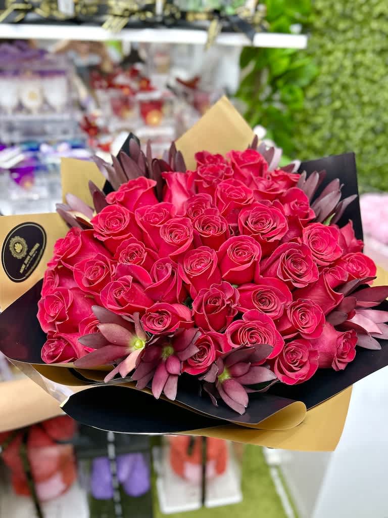 Large bouquet of hot pink roses with purple blooms wrapped in black and gold paper.