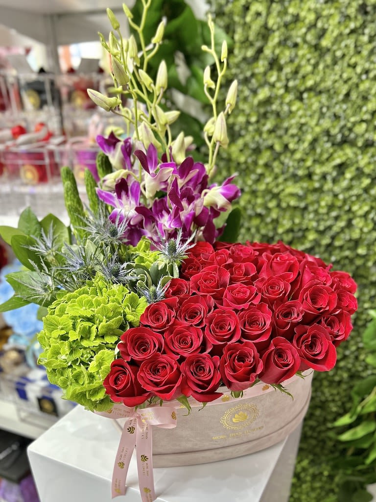 Round hatbox arrangement with red roses, green hydrangeas, and purple orchids