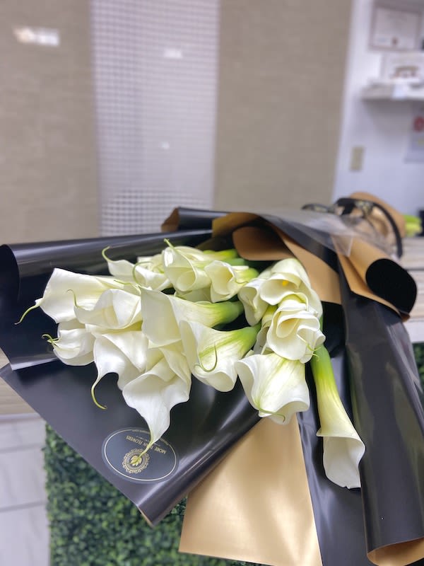 Wrapped bouquet of white calla lilies in black and gold paper on a counter