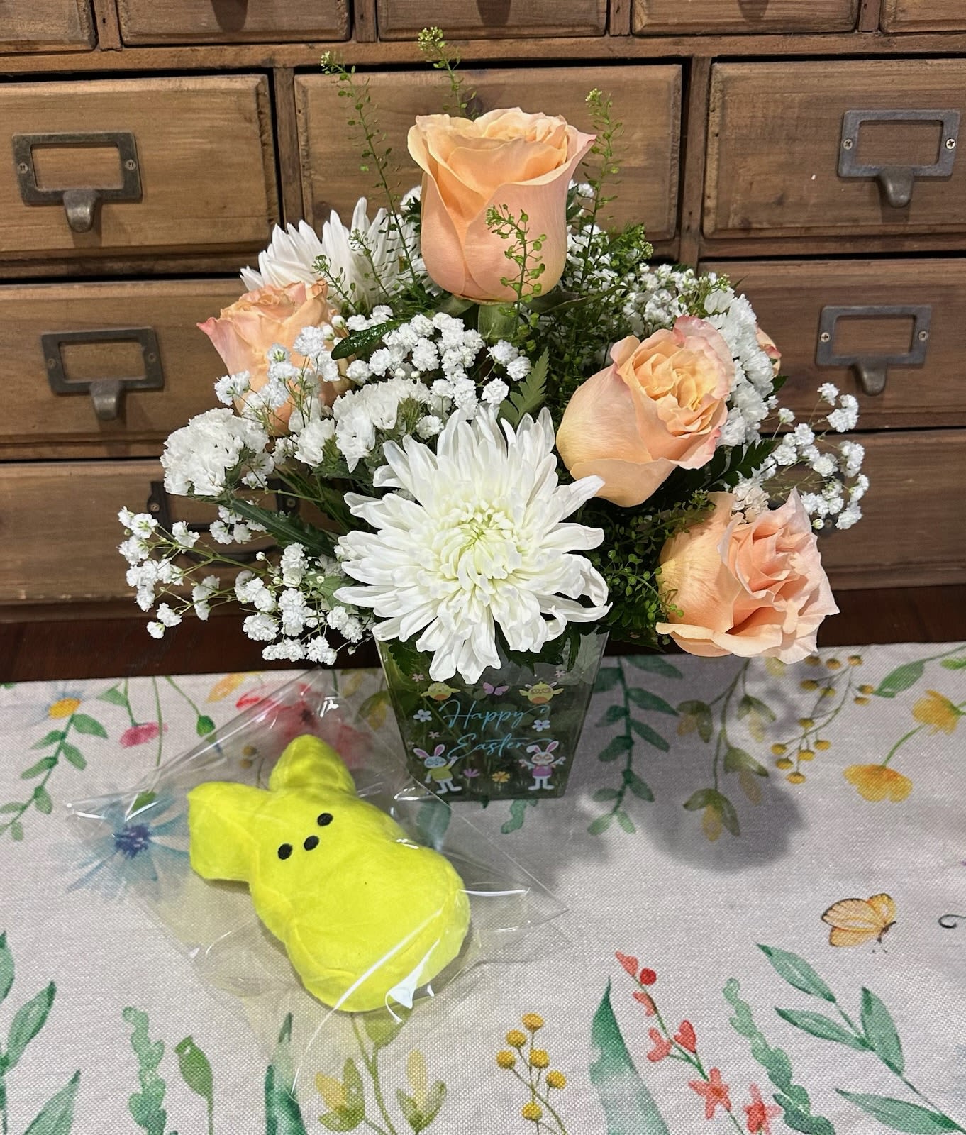 Marshmallow Peep Bouquet  - This Petite Centerpiece bouquet Has beautiful pastel peach shimmer roses, large white mums, white statice and pennycress in a cute Easter themed container.  Each bouquet comes with a plush Peep (color will vary)