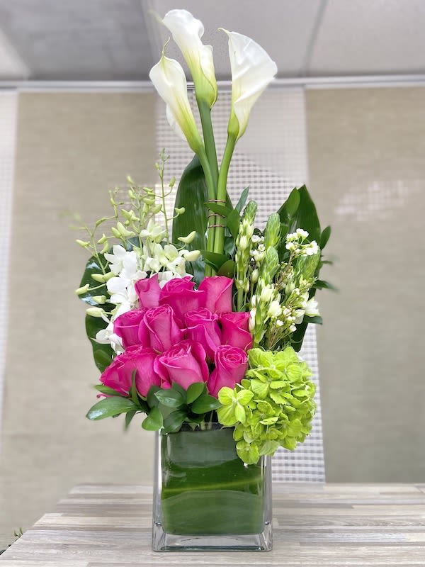 Tall modern arrangement with white calla lilies, hot pink roses, and green hydrangea in a glass cube vase