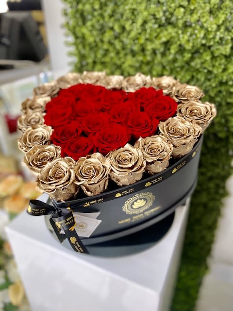 Round black hatbox of red and gold roses with red blooms shaped into a heart.