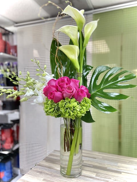 Tall arrangement of white calla lilies, pink roses, green hydrangea and orchids in a clear glass vase