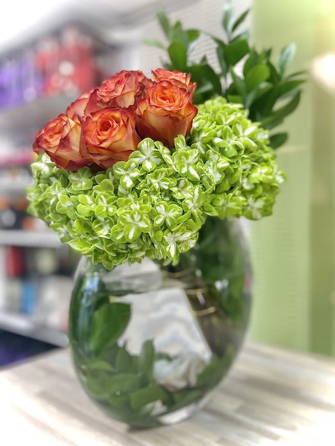 Round glass vase with orange roses and bright green hydrangea blooms