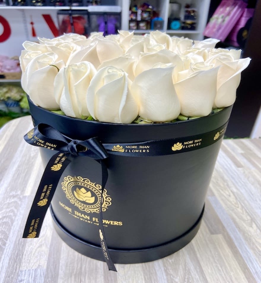 Round black hat box filled with tightly packed ivory roses and tied with a black ribbon