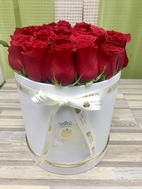 Round white hatbox filled with tightly packed red roses and tied with a cream ribbon bow.