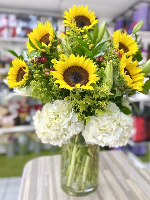 Tall arrangement of yellow sunflowers and white hydrangeas in a clear glass vase