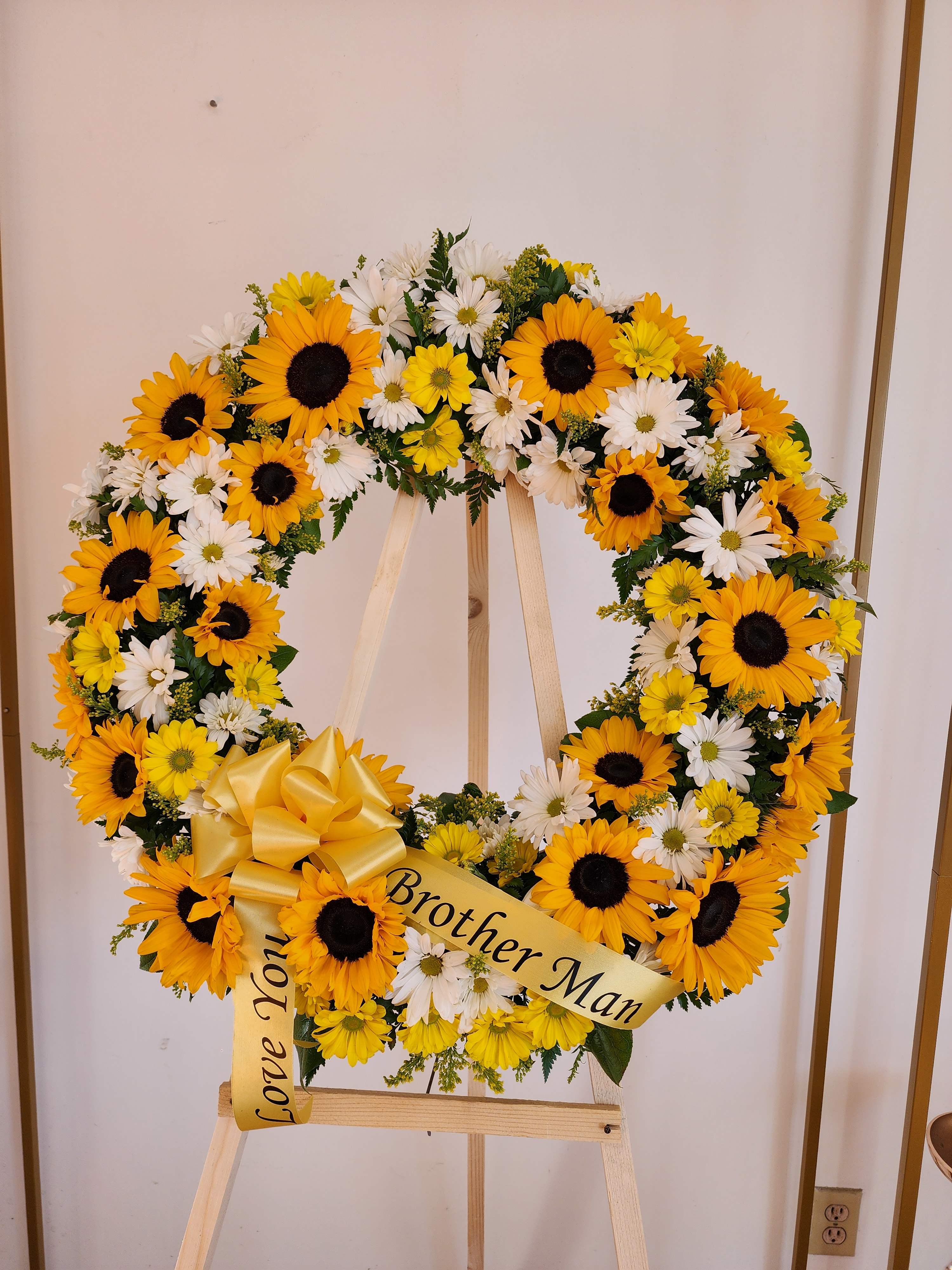 Standing round wreath of yellow sunflowers and white daisies with a yellow bow on an easel