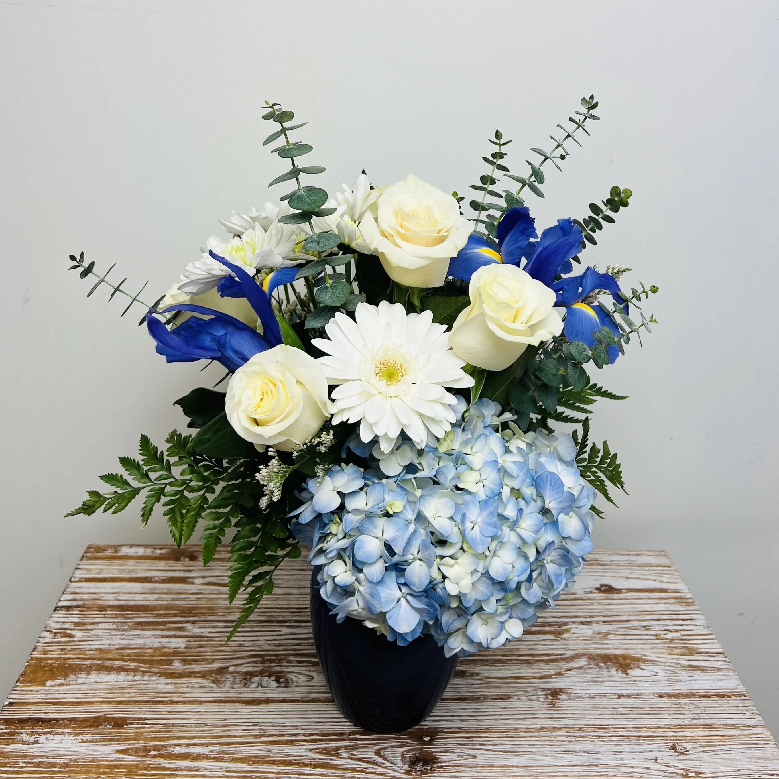 Beautiful in Blue - Fresh blooms of blue and white in a blue glass vase. A popular choice to show your sympathy.  Container Country of Origin: China Flower Country of Origin: Canada, Ecuador, Columbia