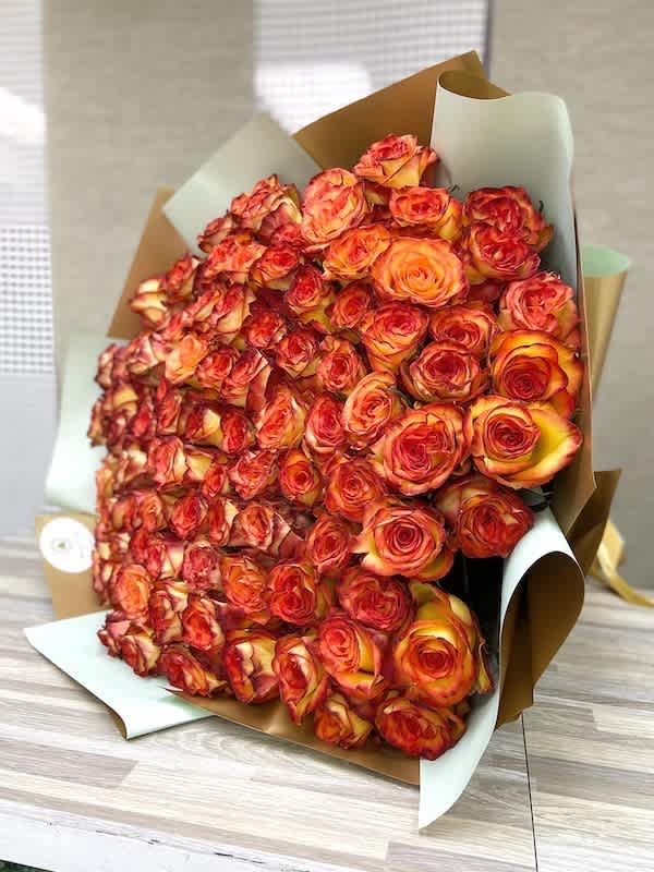 Large wrapped bouquet of tightly clustered orange and red roses on a wooden surface