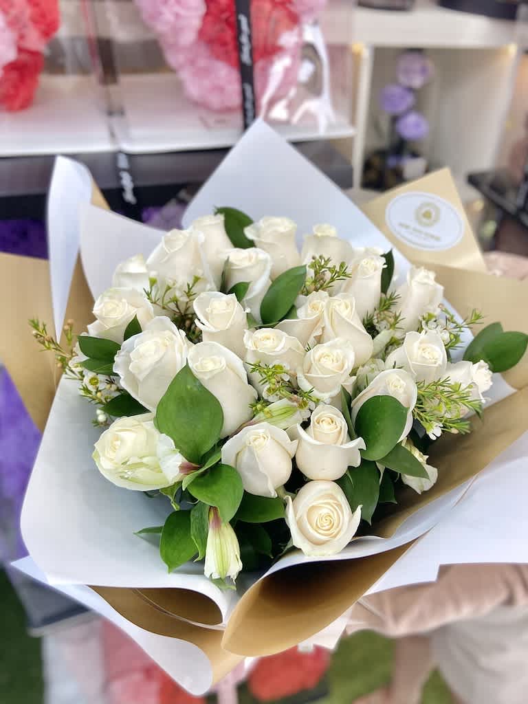 Handheld bouquet of white roses with green accents wrapped in layered white and tan paper