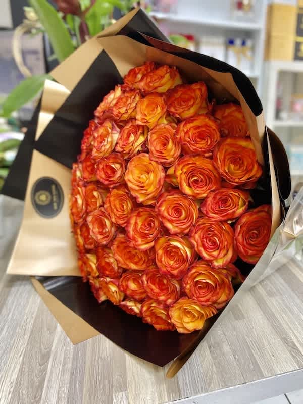 Large bouquet of tightly packed orange and yellow roses wrapped in tan and black paper
