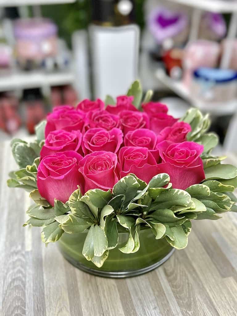 Round arrangement of hot pink roses with a ring of variegated leaves in a low glass vase