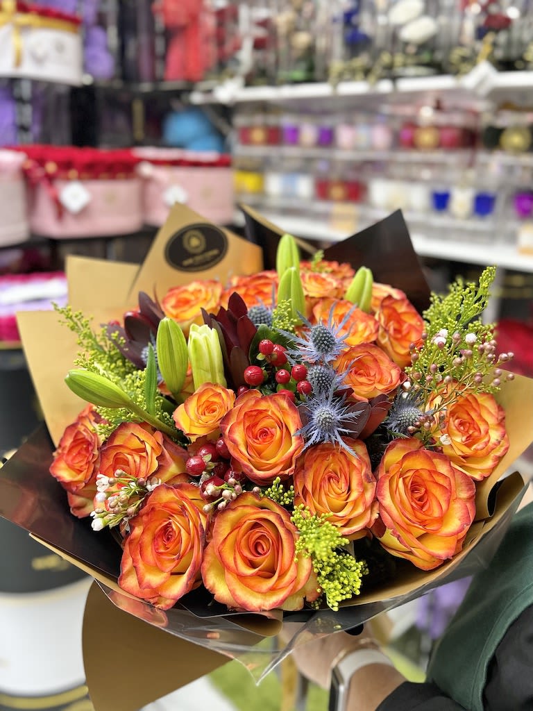 Hand-tied bouquet of orange roses with lilies and accent flowers in decorative wrap