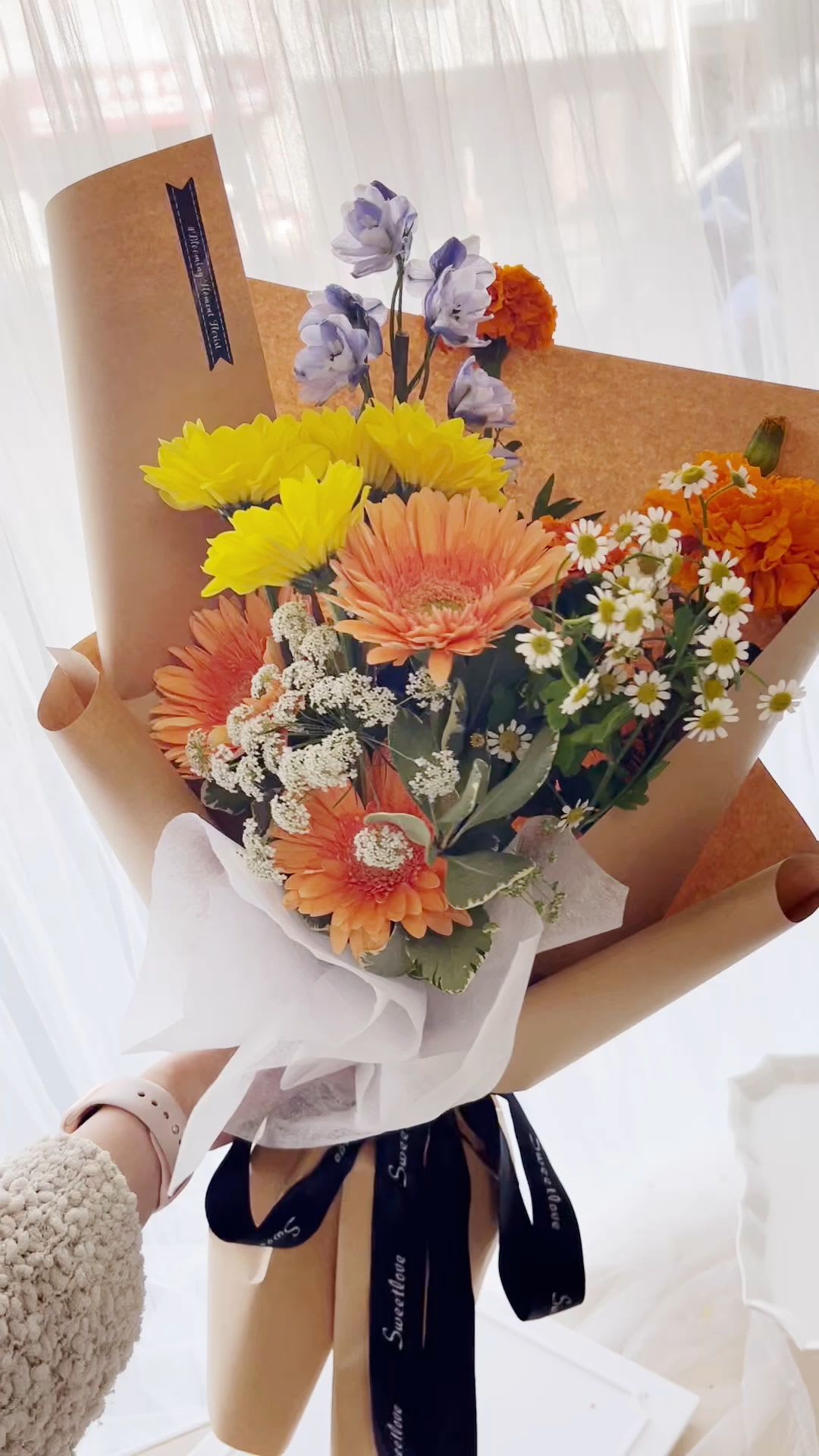 [FRESH FLOWER] Cheery Gerbera - A bright and joyful bouquet designed to bring warmth and positivity. This arrangement features vibrant orange and soft peach gerbera daisies paired with cheerful yellow blooms, creating a lively and uplifting color palette. Accented with delicate white chamomile-style flowers, airy fillers, and subtle lavender tones, it offers a fresh, garden-inspired look with a light and natural feel.  Wrapped in premium kraft paper with a soft Korean-style finish and tied with an elegant ribbon, this bouquet is perfect for sending happiness, encouragement, or a thoughtful surprise.