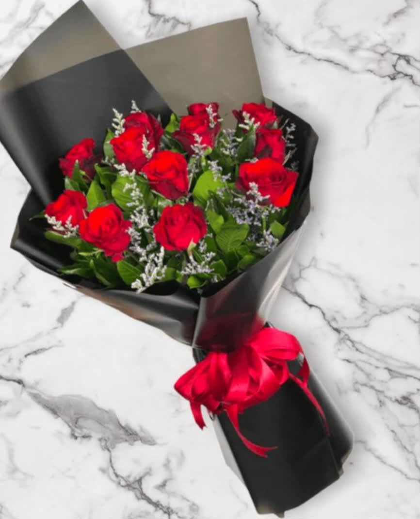 Bouquet of red roses with white filler flowers wrapped in black paper and tied with a red ribbon