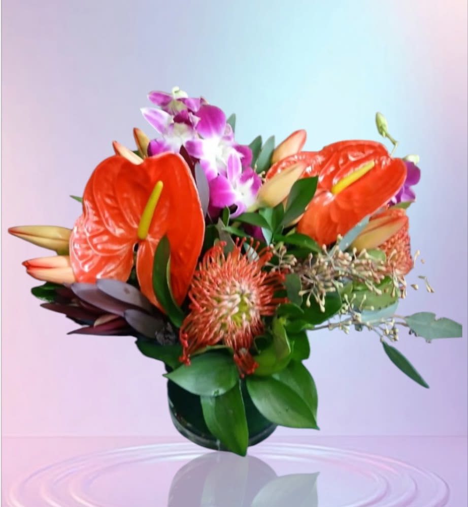 Tropical arrangement with orange anthuriums, pincushion protea, lilies, and purple orchids in a low glass vase