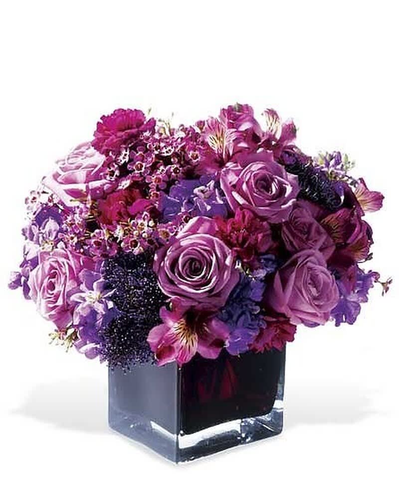 Compact arrangement of purple and pink flowers in a square glass vase