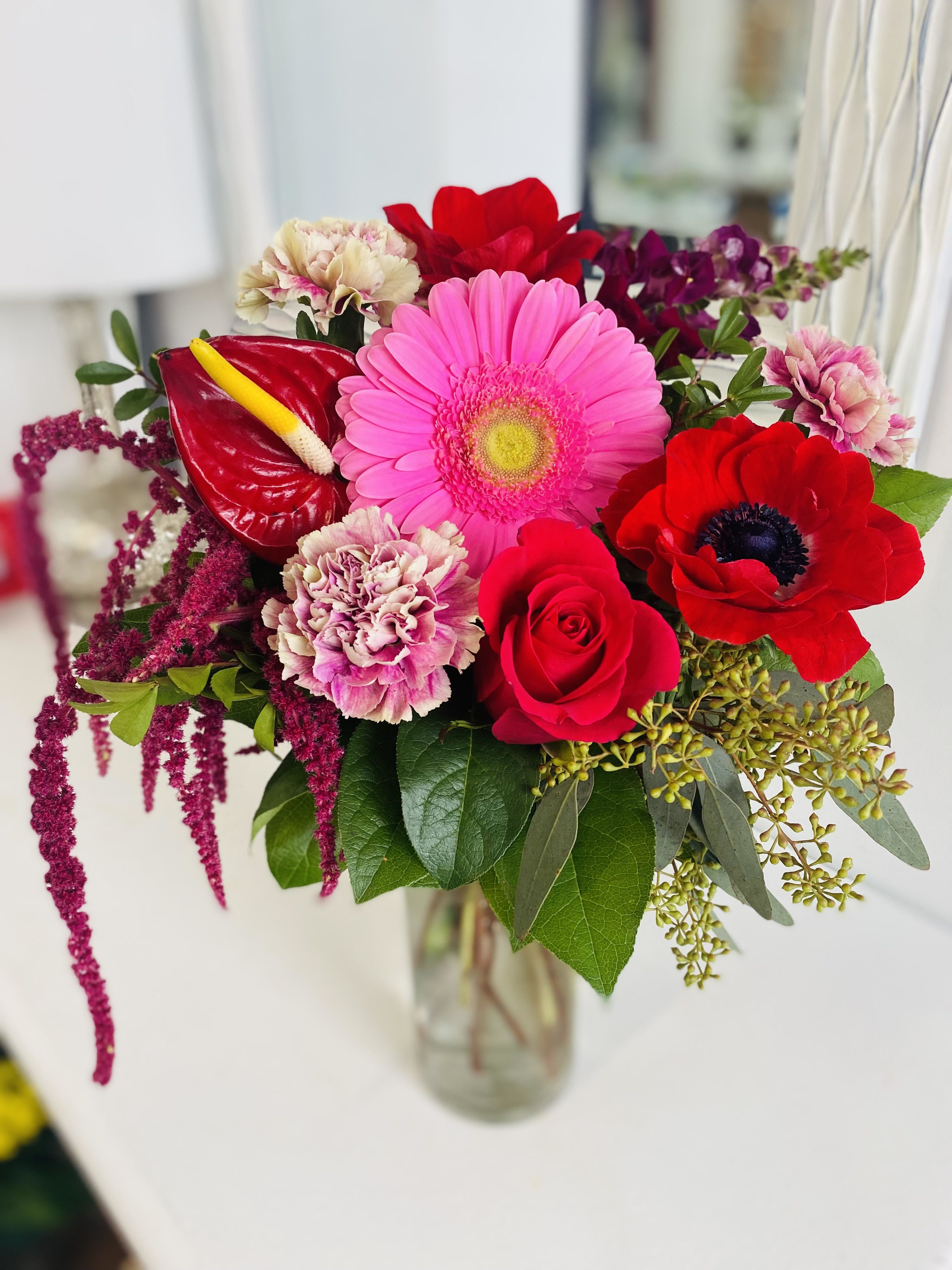 Bright bouquet of pink gerbera, red rose, carnations and anthurium in a clear glass vase