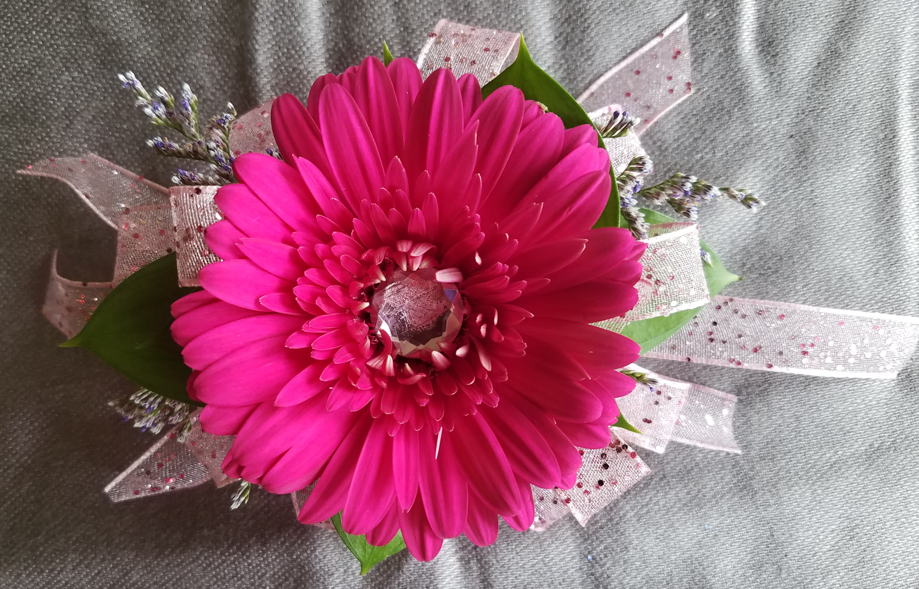 Corsage Gerber Daisy  - This corsage has a Gerber Daisy including a center rhinestone with greens and filler. We have all sorts of ribbon from lime green sparkle to animal print, just tell us in the special instructions what your looking for! You may also send us a picture of your dress or inspirations to our email address lvfloral@gmail.com just make sure to include your name and order number.     ALL corsage/boutonniere orders will be ready for PICK UP ONLY between 1pm-4pm the day of the event. 
