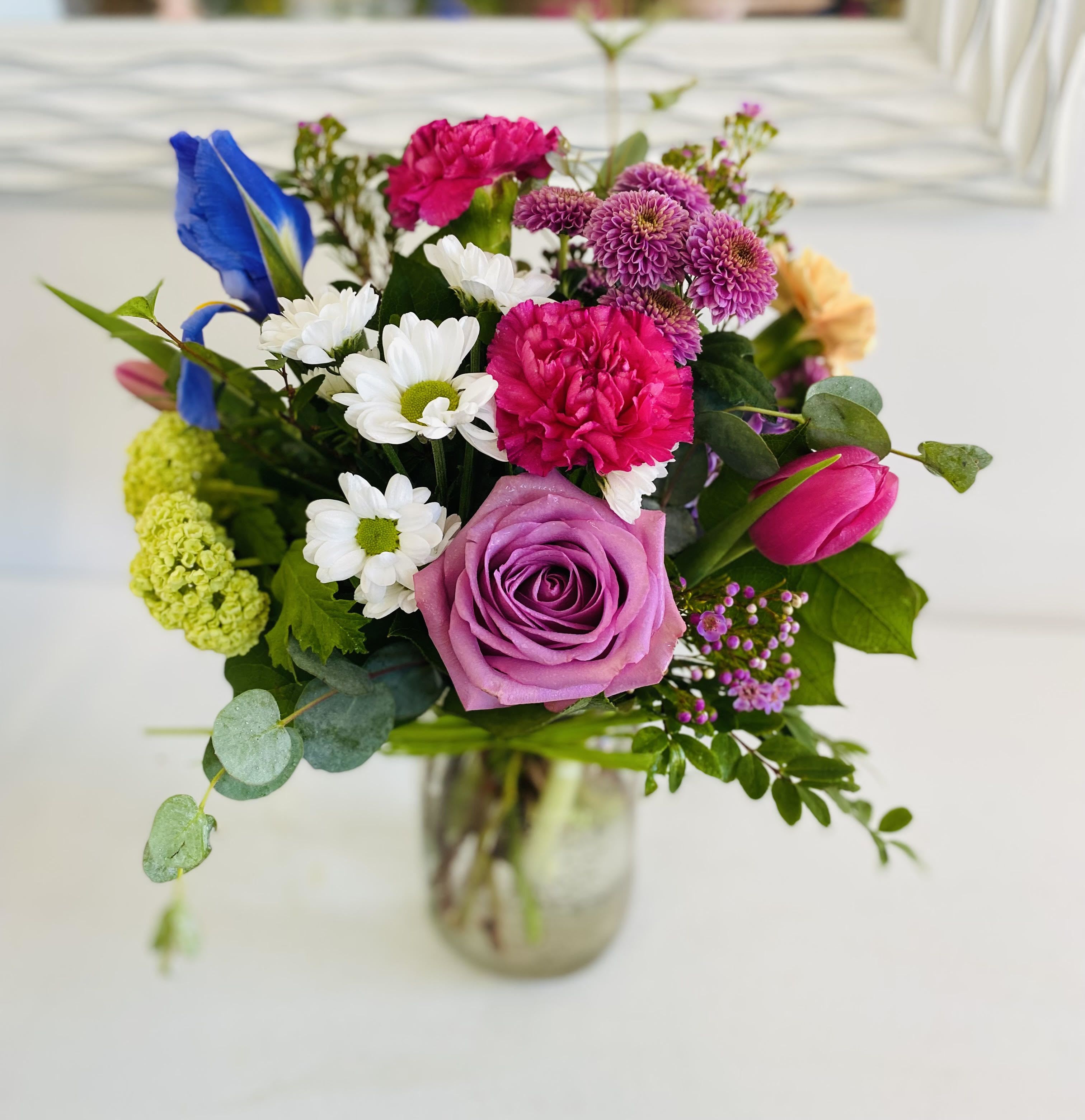 Colorful mixed bouquet with pink rose, carnations, daisies, tulip and iris in a clear glass jar vase