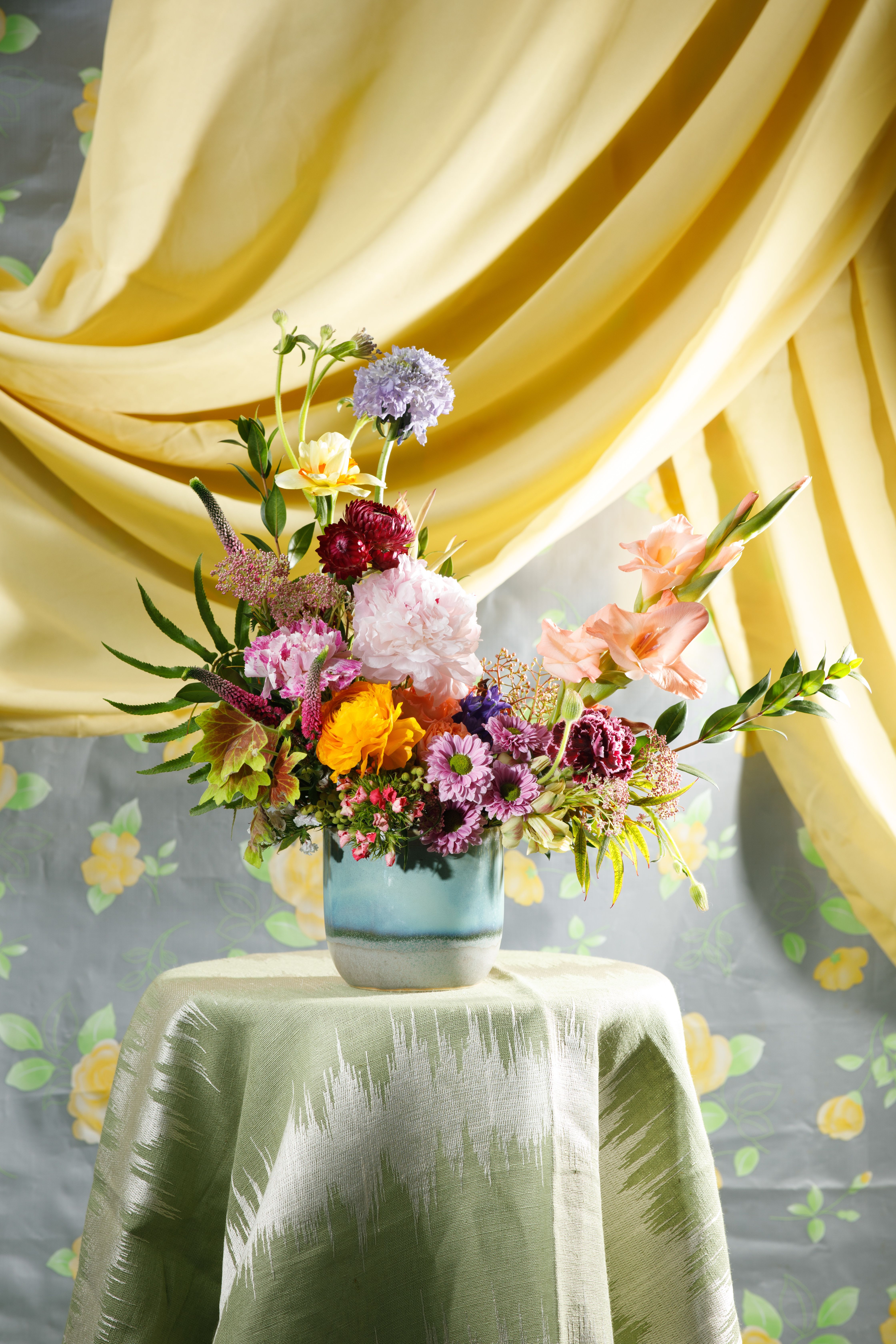 Bed-Stuy Collection: The Marcy , Spring/Summer Edit   - "The Marcy” is our one-sided style arrangement created in one of our hand-picked ceramic vessels.  With “The Marcy’s” one-sided design it is the perfect fit for your mantle or any shelf in your space.   Note: This is a one-sided arrangement, it’s created with placement in mind. The Marcy is for a place where one side of the arrangement will face a wall. (i.e. mantle or shelf)   Each of our custom designs is created using fresh curated seasonal blooms and foliages. Designers will choose from a unique array of flowers to create an arrangement tailored for you. For special floral requests please place an order 4 days prior to the desired delivery date.    **Please note that Brooklyn Blooms move with the seasons, vessels, blooms, and foliage will vary from what you see in the photo. However, it will have the same beauty, uniqueness, and funky style. Please let us know in the florist notes if you have any color preferences or special requests. If you like what you see in the photo please let us know in the florist notes and the designers will use it as inspiration. Otherwise, the Bloomies will make a tasteful decision for you!**  ***ALL SPECIAL REQUESTS MUST BE SPECIFIED IN THE FLORIST NOTES SO THAT OUR BLOOMIES ARE AWARE AND CAN DELIVER THE BEST SERVICE. COMMUNICATION IS KEY!!****  Upgrade Notes: Please note that with each upgrade the Bloomies will choose a mix of blooms, premium foliages, and filler to enhance your arrangement for the best presentation!  