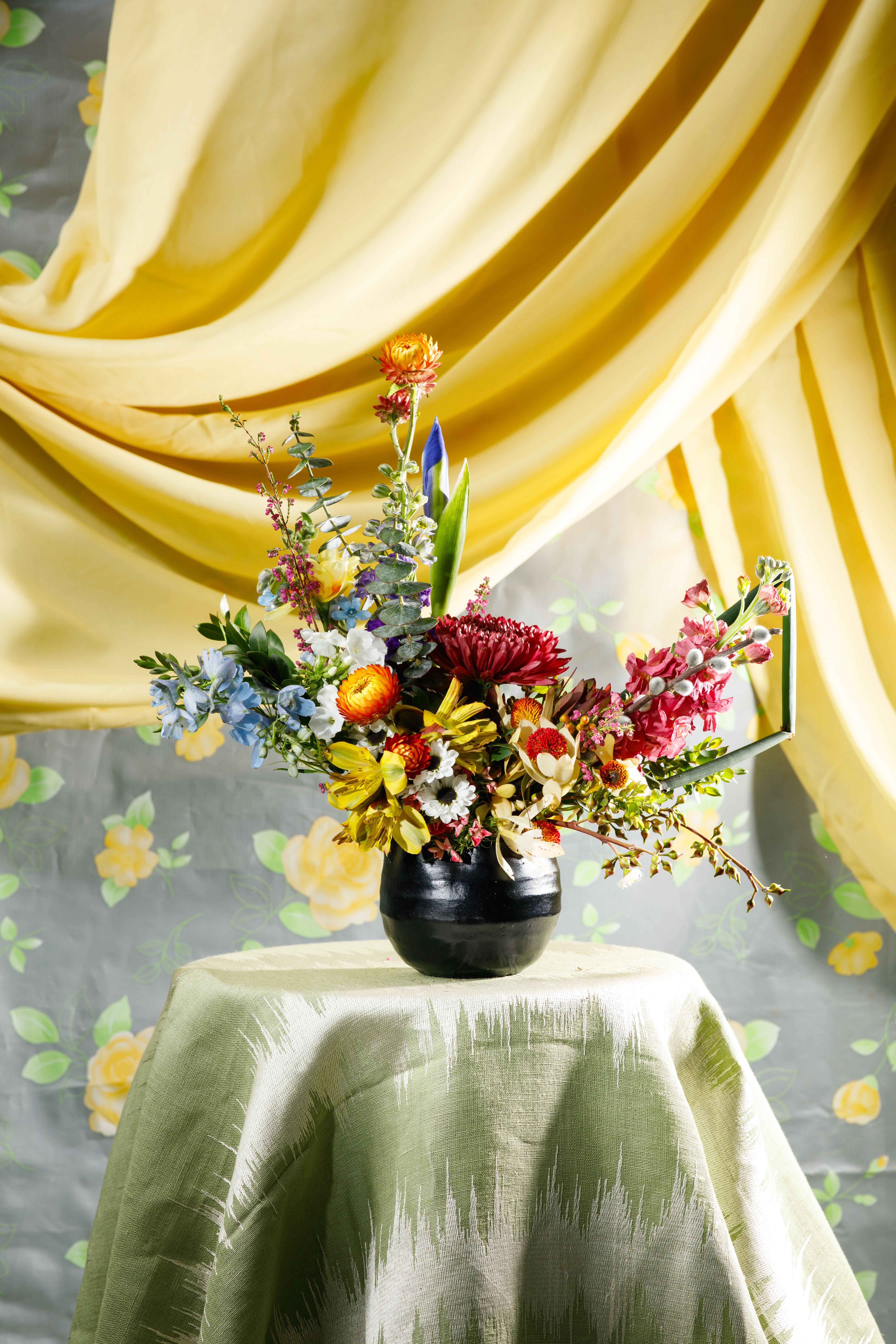 Bed-Stuy Collection: The Chauncey (For Him), Spring/Summer Edit  - Give him something unexpected and offbeat with this carefully curated arrangement “The Chancey” it is created with him in mind using bold textures, deep hues, and unique blooms for your husband, boyfriend, friend, or that special guy in your life.   Each of our custom designs is created using fresh curated seasonal blooms and foliages. Designers will choose from a unique array of flowers to create an arrangement tailored for you. For special floral requests please place order 4 days prior to the desired delivery date.   **Please note that Brooklyn Blooms move with the seasons, vessels, blooms, and foliage will vary from what you see in the photo. However, it will have the same beauty, uniqueness, and funky style. Please let us know in the florist notes if you have any color preferences or special requests. If you like what you see in the photo please let us know in the florist notes and the designers will use it as inspiration. Otherwise, the Bloomies will make a tasteful decision for you!**  ***ALL SPECIAL REQUESTS MUST BE SPECIFIED IN THE FLORIST NOTES SO THAT OUR BLOOMIES ARE AWARE AND CAN DELIVER THE BEST SERVICE. COMMUNICATION IS KEY!!****  Upgrade Notes: Please note that with each upgrade the Bloomies will choose a mix of blooms, premium foliages, and filler to enhance your arrangement for the best presentation!  